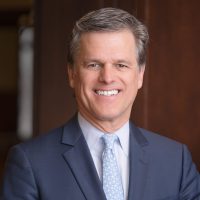 Color photograph of CASEL Board chair, Tim Shriver, smiling and wearing a gray suit and light blue tie with a pattern of small white flowers.